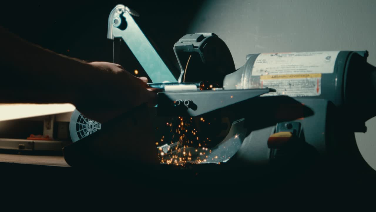 골프 클럽 제작자가 어두운 작업실에서 철을 길이로 자르고, 4k에서 날아다니는 불꽃으로 가까이 다가옵니다.
