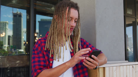 Mixed-race-man-with-dreadlocks-sitting-at-table-outside-cafe-using-smartphone