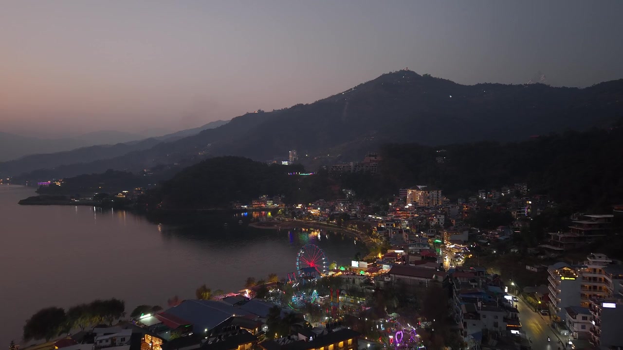 Perspectiva de dron del paisaje urbano de Pokhara al anochecer con luces vibrantes de la ciudad y ambiente costero.