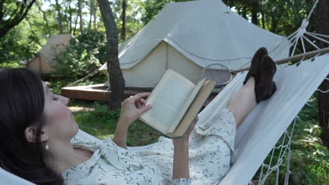 chica con cabello oscuro en vestido de campo blanco lee un libro en una hamaca