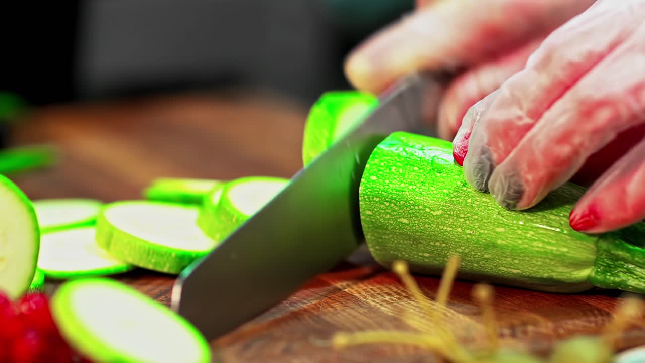 Slicing green zucchini on wooden cutting board with gloved hands