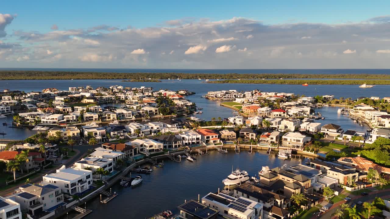 Drone footage captures luxury waterfront estates and boats at Gold Coast, Australia, under clear skies and warm lighting
