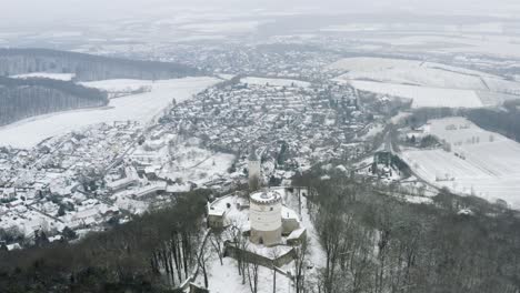 Antena-De-Drones-Del-Castillo-De-Cuento-De-Hadas-Plesse-En-Invierno-Con-Una-Gran-Cantidad-De-Nieve-En-Una-Hermosa-Montaña-Cerca-De-Bovenden,-Alemania,-Europa