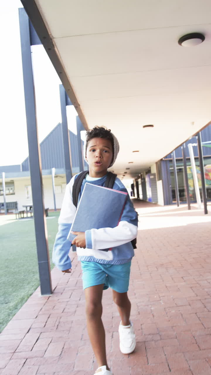 Vertical video: In school, child running with backpack and notebook in outdoor hallway