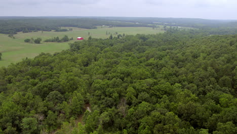 Push-forward-over-lush-green-trees,-fields-and-pastures-and-towards-a-red-barn-in-Farmington-in-southern-Missouri-on-a-cloudy-summer-day