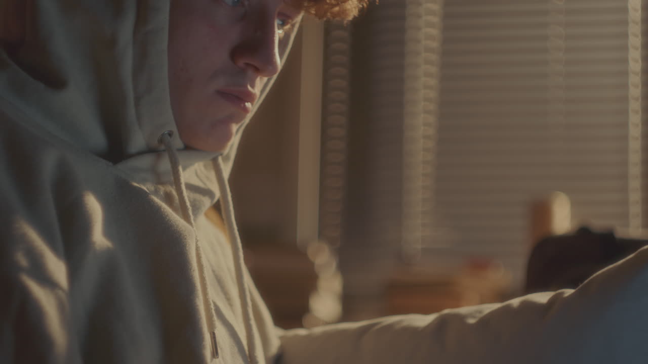 집에서 노트북으로 타이핑하는 후디를 입은 집중된 젊은 남자