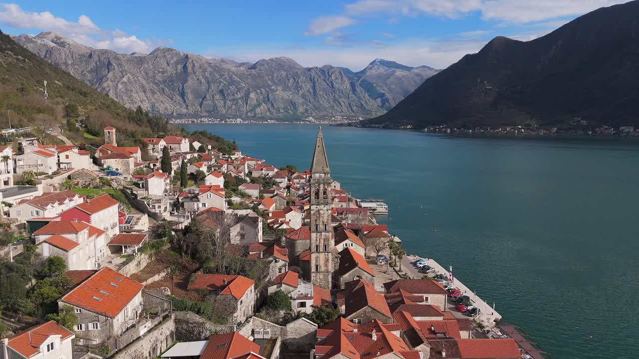 4K drone footage captures Saint Nicholas Church in the charming town of Perast, Montenegro, with a beautiful view of the UNESCO-listed turquoise Bay of Kotor and mountains in the background