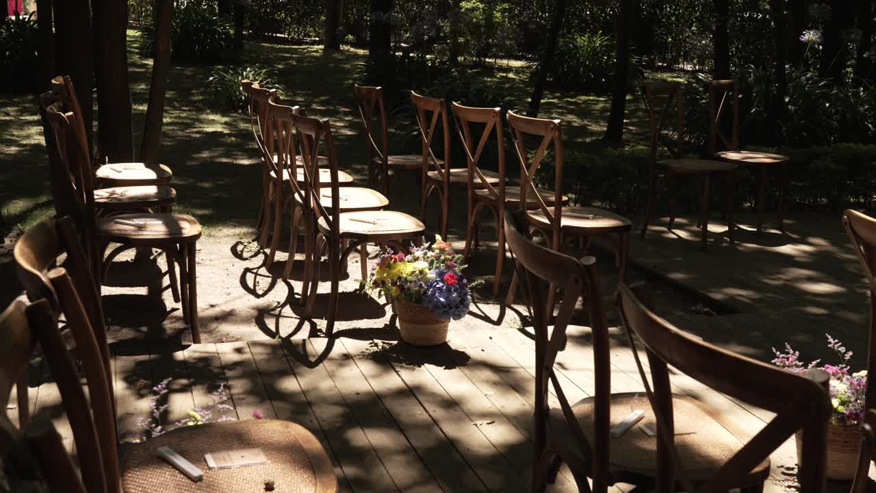 Wooden chairs arranged for an outdoor wedding ceremony with floral decorations