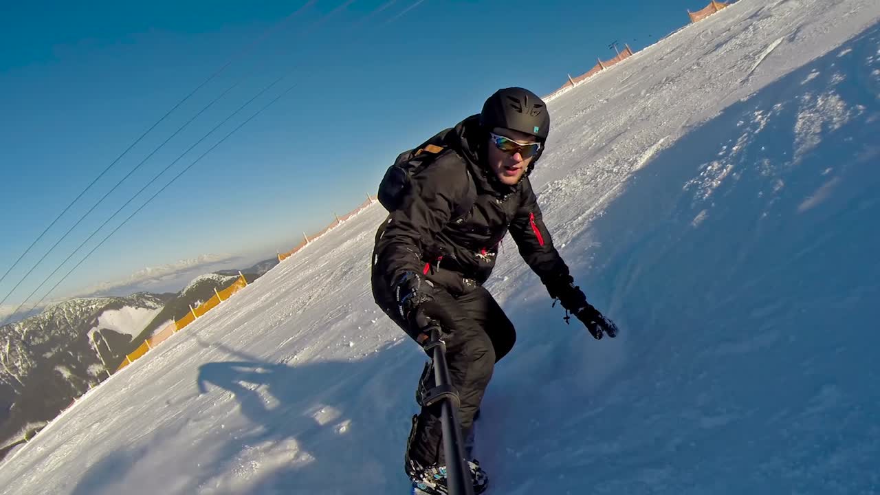 vista frontal de un snowboarder bajando a alta velocidad con un selfie stick y casi cayendo