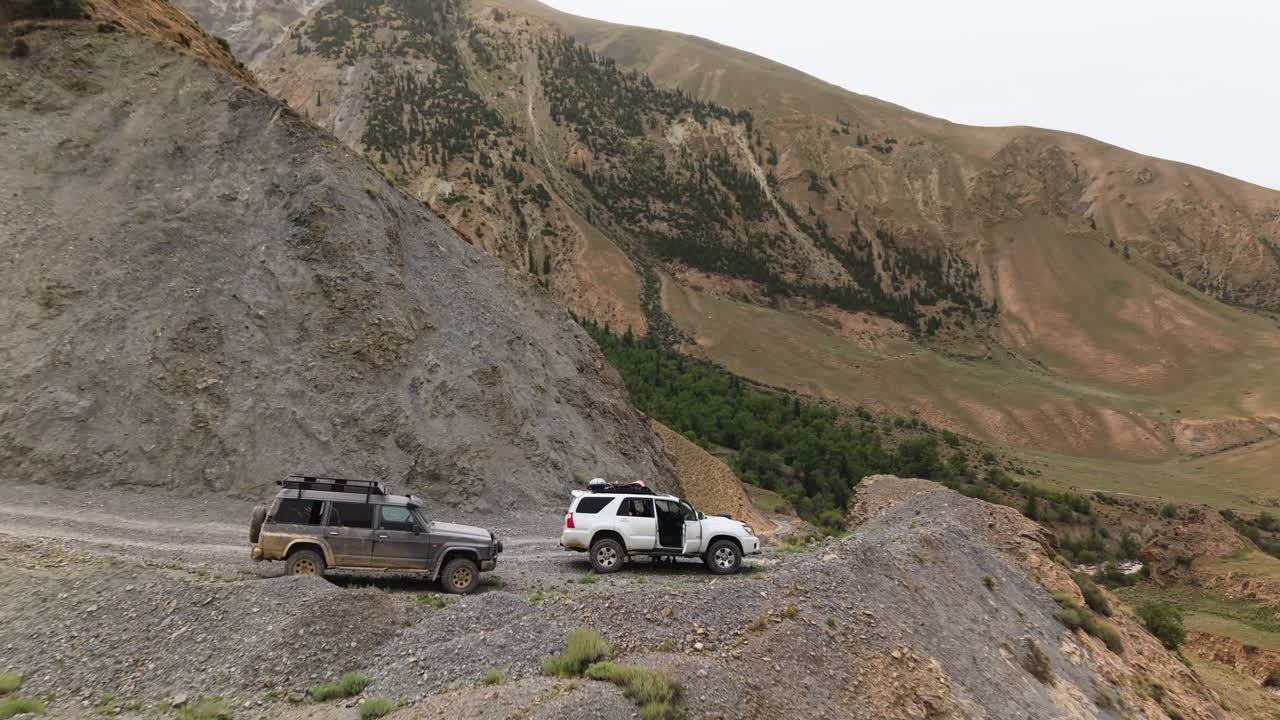 SUV Vehicles Over Cliffside Roads In Mountainous Landscape Of Kyrgyzstan, Central Asia. Aerial Pullback Shot