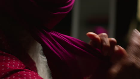 close up low key studio lighting shot of senior sikh man with beard tying fabric for turban against dark background 4