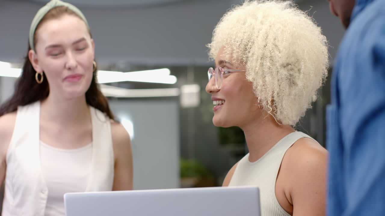 Discussing project and using laptop, diverse colleagues collaborating in office