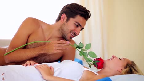 hombre cosquilleando a su novia con una rosa roja en la cama