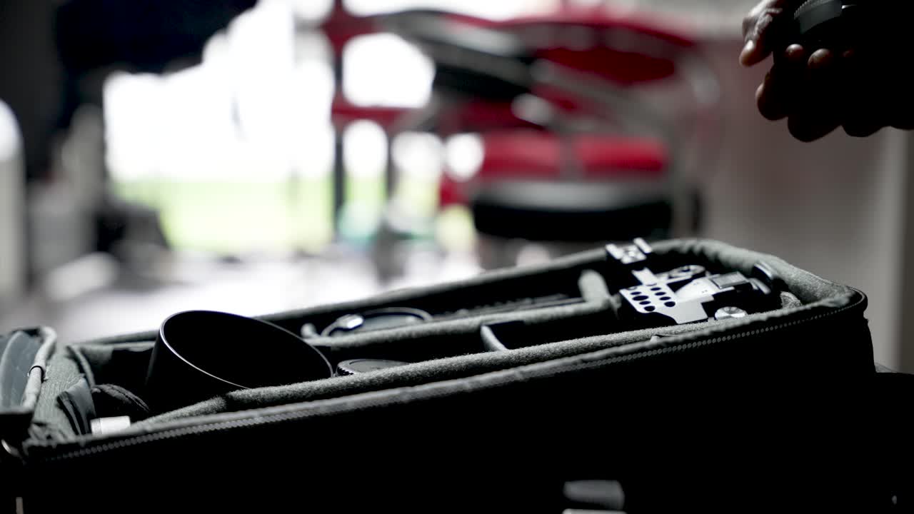 A photographer's hand reaches a lens in a compact indoor camera bag, ready for shoot