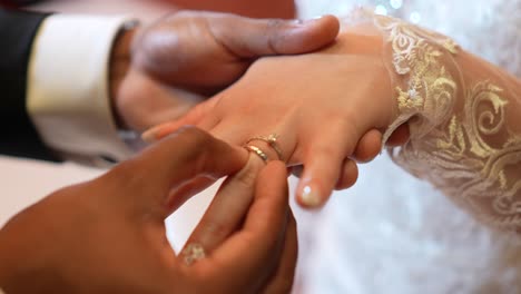 Groom-placing-the-wedding-ring-on-his-bride-during-their-wedding-ceremony