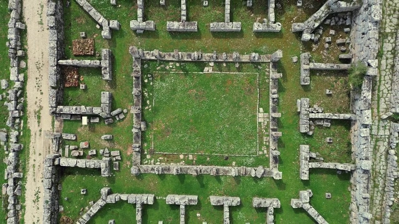Cinematic 4K drone top-down ascending shot over the geometric stone ruins of the ancient Prytaneum in Kassope, Greece. Perfect symmetrical abstract archaeological layout.