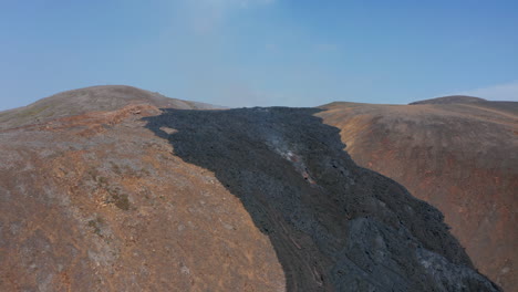 Otherworldly-Icelandic-Fagradalsfjall-landscape.-Aerial-drone-flying-forward-towards-black-lava-river-flowing-between-mountains,-drone-lower-near-smoky-lava,-day