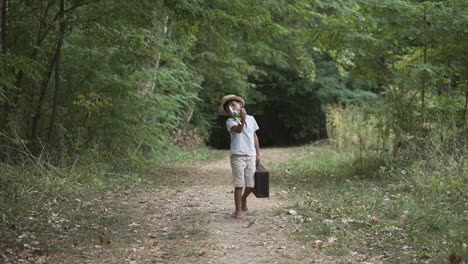 boy in the forest walking towards the camera carrying a suitcase and playing with a toy airplane