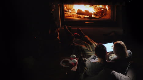 a young couple uses a tablet in their house by the fireplace a nice evening together