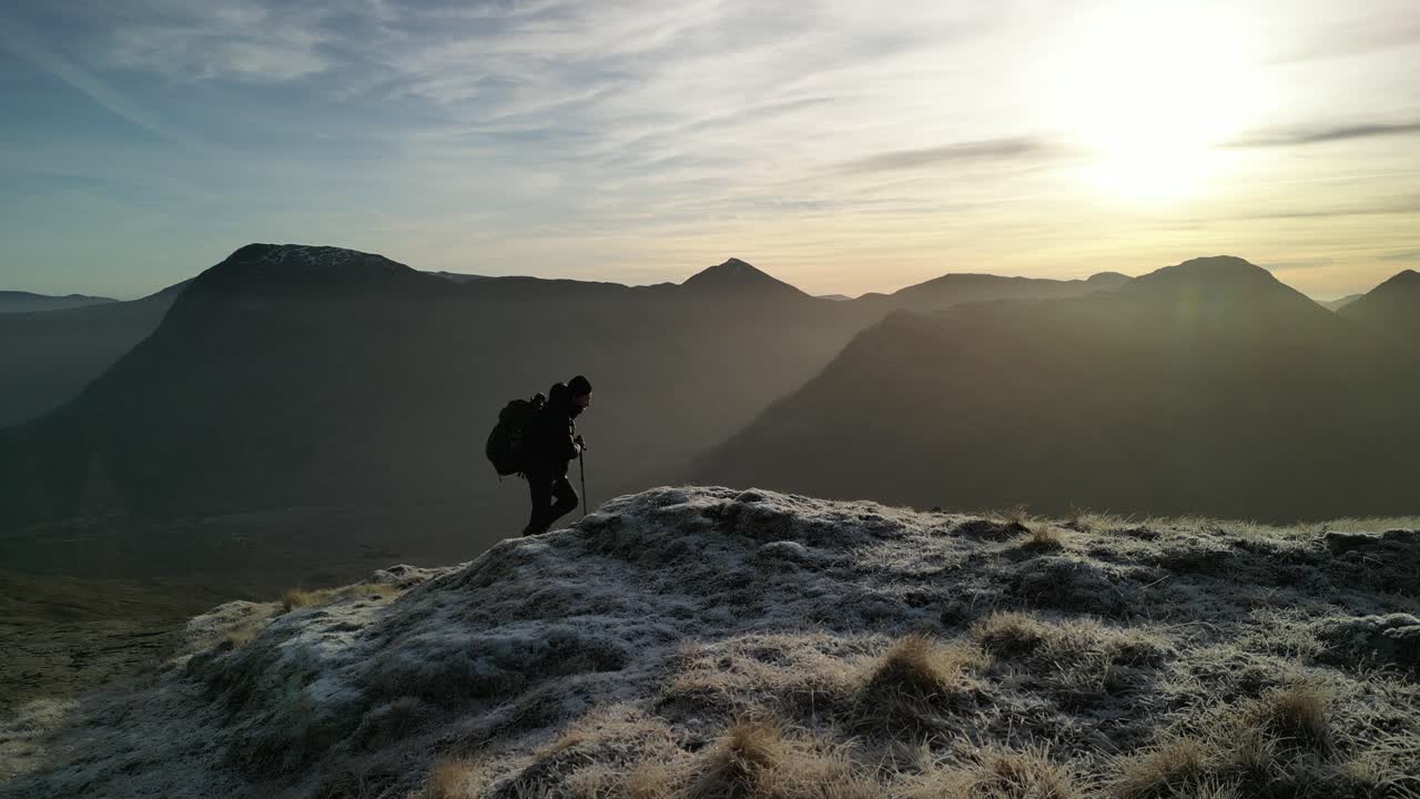 Glen Coe, Highlands scozzesi: ripresa aerea invernale delle montagne, con escursionista che attraversa l’inquadratura - carrellata