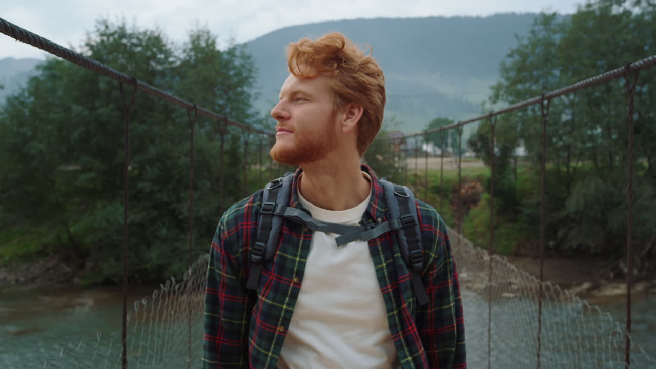 Hiker walking mountain valley bridge. Redhead guy enjoying adventure outside.