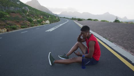 Hombre-Afroamericano-Sosteniendo-Un-Teléfono-Inteligente-Tomando-Un-Descanso-De-Correr-En-La-Carretera