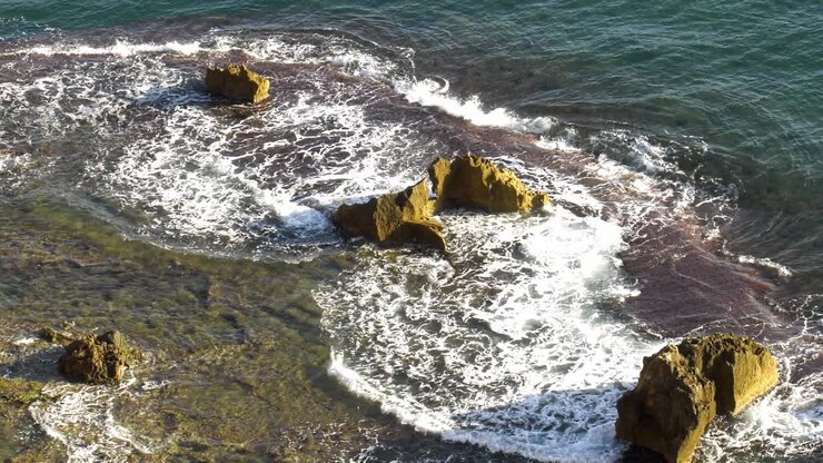 Bellissimo paesaggio marino con onde blu che si infrangono sulla barriera corallina con isolotti rocciosi, ripresa dall'alto, slow motion