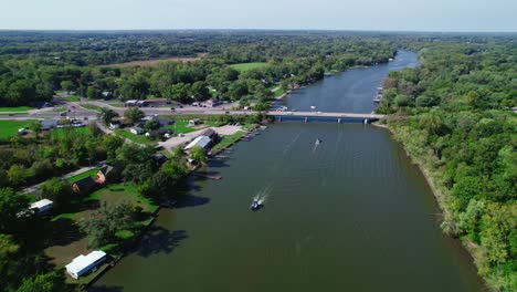 Vista-Aérea-Del-Paisaje-Sobre-El-Río-Fox-Con-Barcos-Pasando-Y-Un-Puente-Con-Algo-De-Tráfico,-Crystal-Lake,-Illinois.