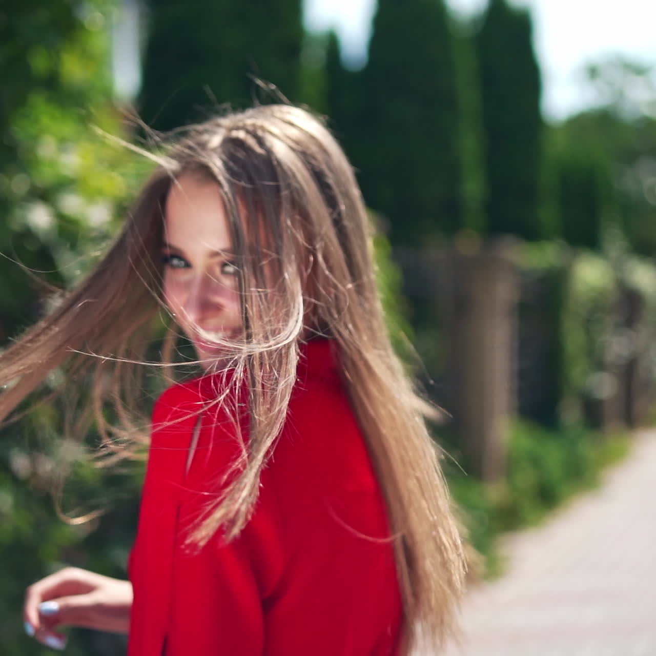 Attractive girl outdoors in summer. Long-haired woman in passionate red dress looking on camera and smiling in the city street. Slow motion.