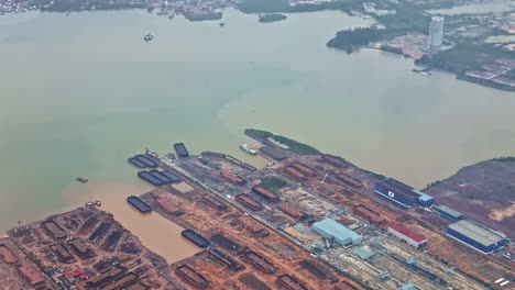 expansive aerial shot of a malaysian port shipyard with barges, docks, and muddy shoreline, captured from an airplane window