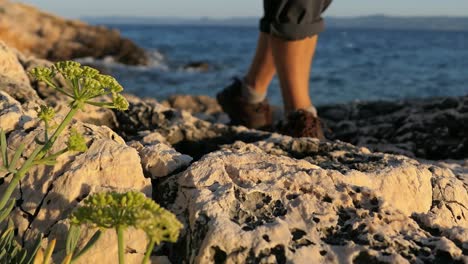 Man-walking-on-rocky-shoreline-by-the-sea,-peaceful-contemplating-walk-in-nature