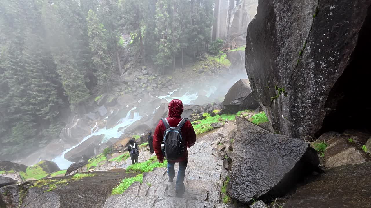 Wanderer steigt felsigen Pfad zu majestätischem Wasserfall hinab