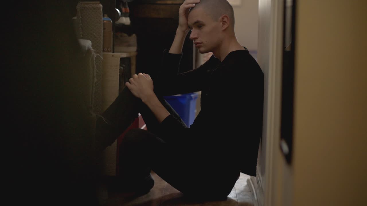 Depressed Caucasian Man Sitting On The Floor In The Stockroom - full shot