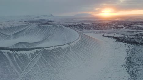 breathtaking drone footage of snowy tephra cone or tuff ring volcano during beautiful sunrise in background - cold frozen winter day on iceland showing hverfjall volcano system reserve