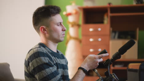 man adjusting video camera with microphone in creative home studio. focused on preparing equipment with green wall and furniture in background, bright natural light shining in workspace