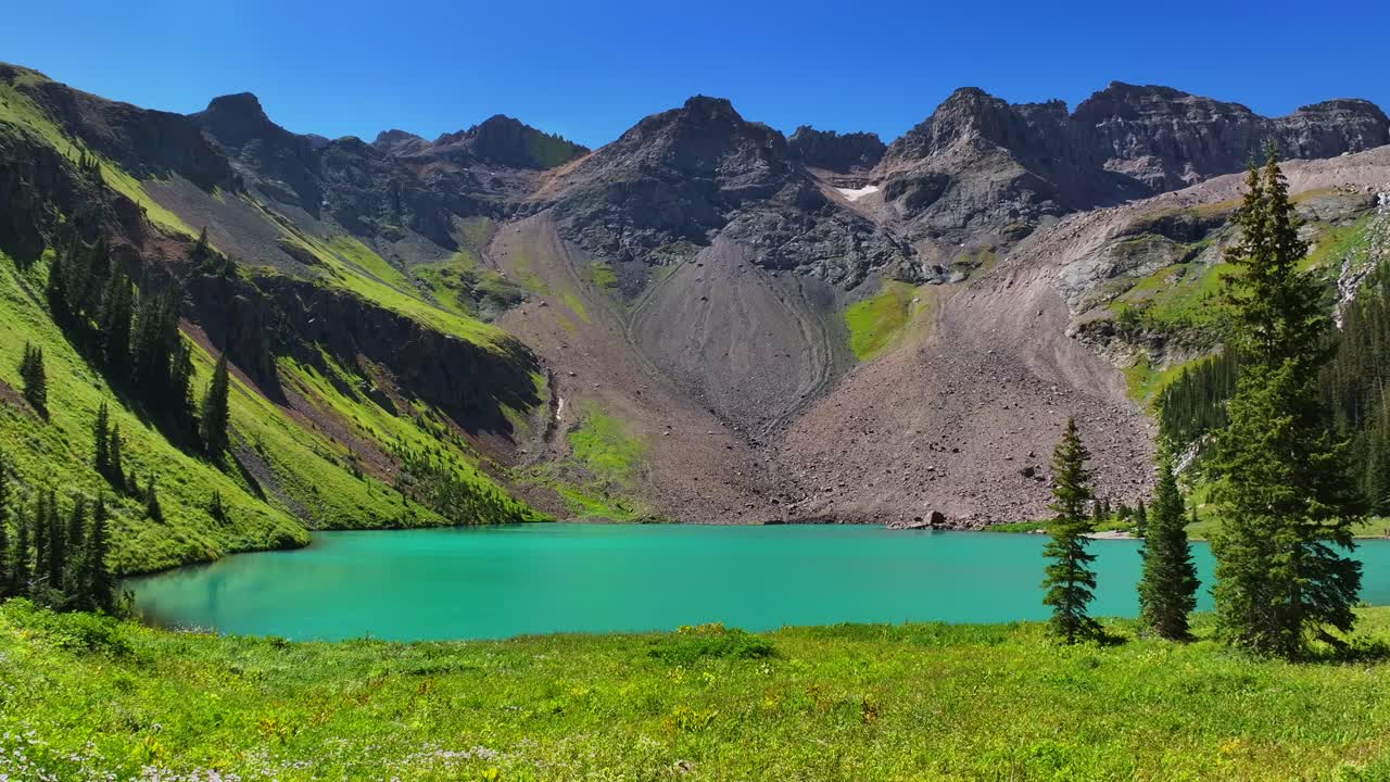 Windy wildflowers Lower Blue Lake Mount Sneffels Wilderness beautiful sunny morning Ridgway Telluride Colorado aerial drone San Juan Rocky Mountains Dallas Range blue sky hiking trails forward pan up