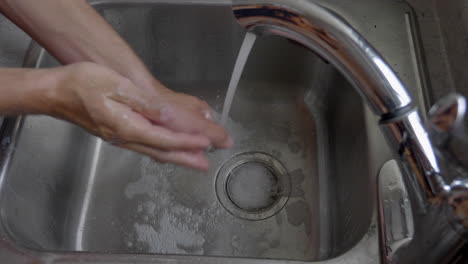 person's hand washing under clean tap water from a faucet - high angle shot