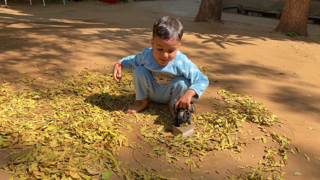 young kid exploring nature while playing with leaves on ground