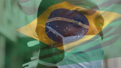 Animation-of-flag-of-brazil-waving-over-african-american-man-wearing-face-mask-in-city-street