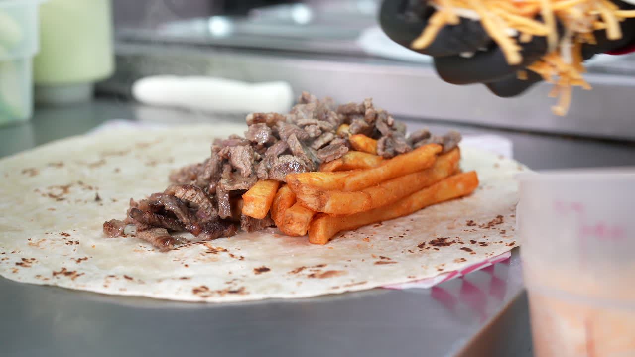 agregando queso al bistec y papas fritas en un burrito californiano - serie de camiones de comida
