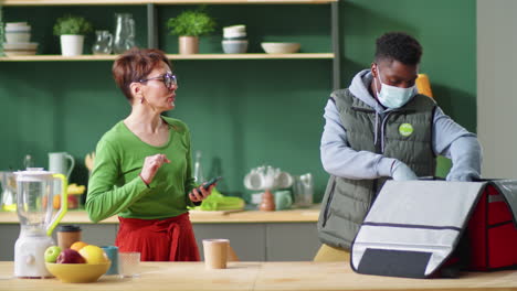 repartidor negro con máscara y guantes descargando cajas de alimentos en la casa del cliente