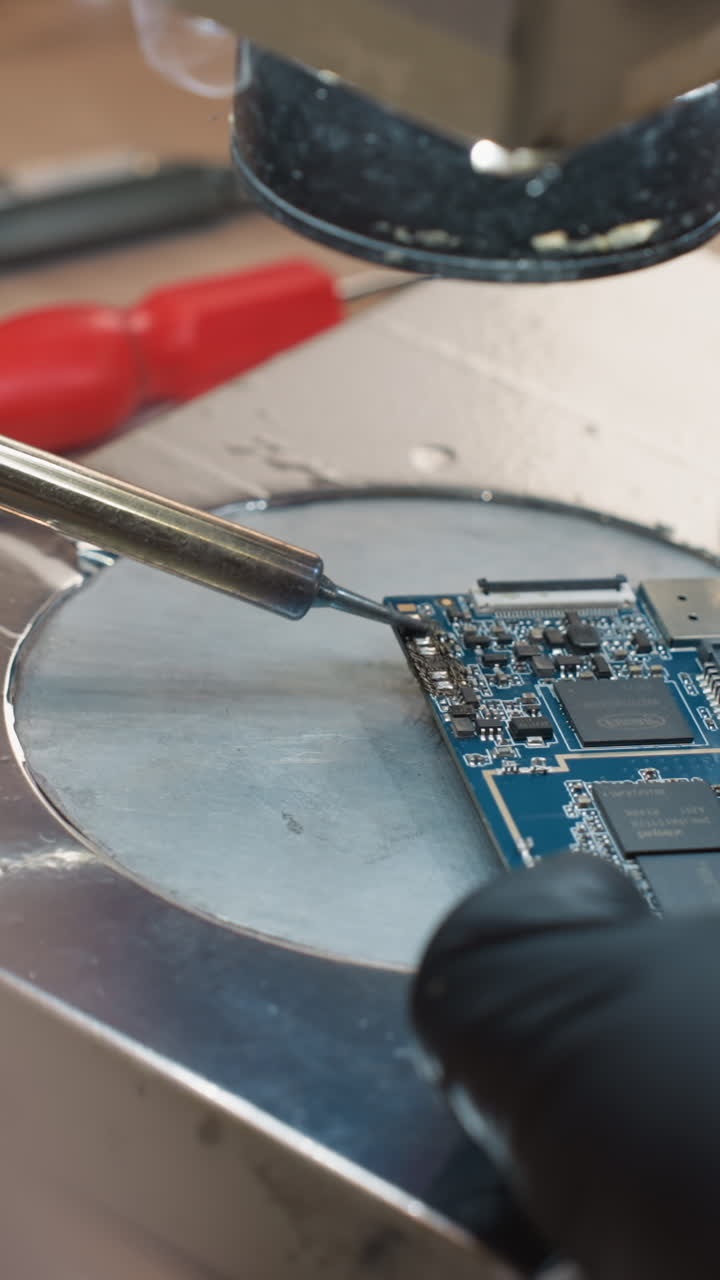 una vista de cerca de una mano de técnico soldando una placa de circuitos impresos (pcb) con un soldador en un taller de reparación electrónica con otras herramientas cercanas