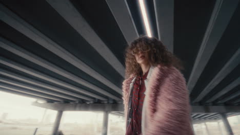 cool girl in trendy outfit dancing and posing on camera under urban overpass