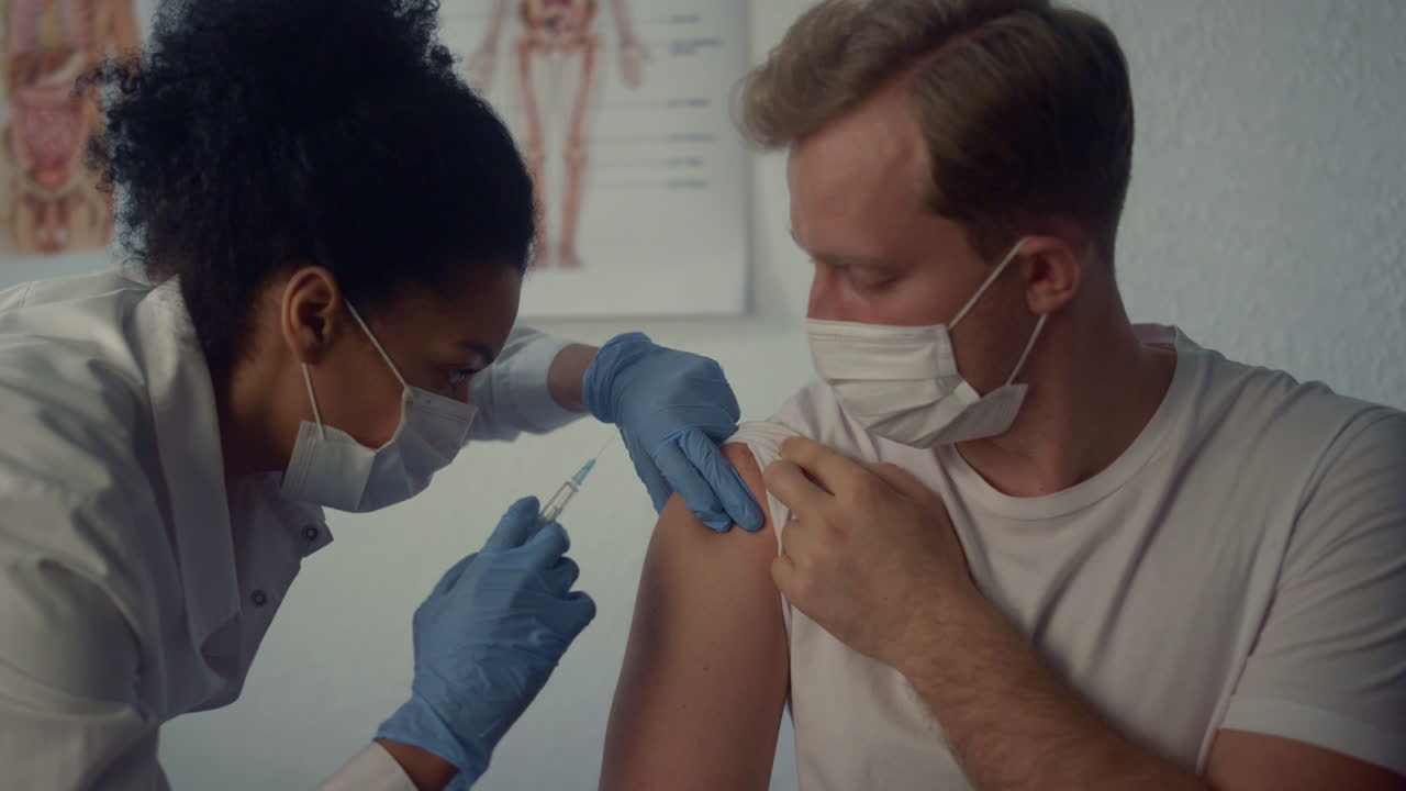 Woman medic injecting covid vaccine in man shoulder. Physician using syringe.
