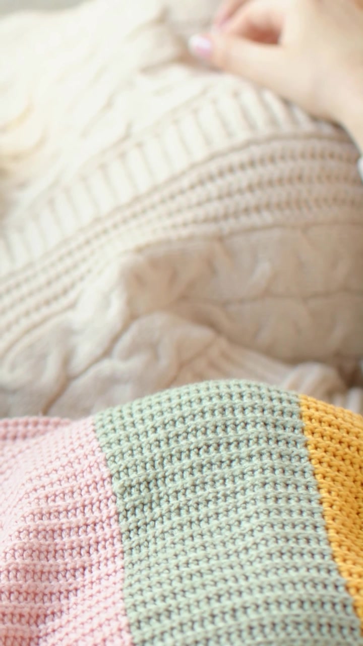 Video verticale: Entrando nell'inquadratura, mano di donna che liscia un plaid color crema sul letto, sistemando una coperta pastello