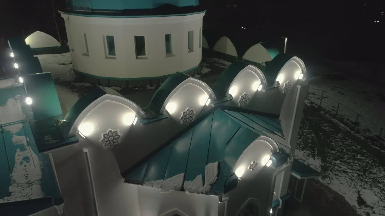 지붕에 눈이 쌓인 놀라운 모스크와 밤에 반이는 램프