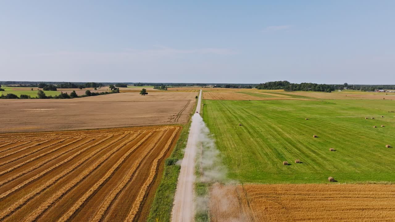 Drone shot of dirt road through fields with vehicle rushing ahead in summer heat