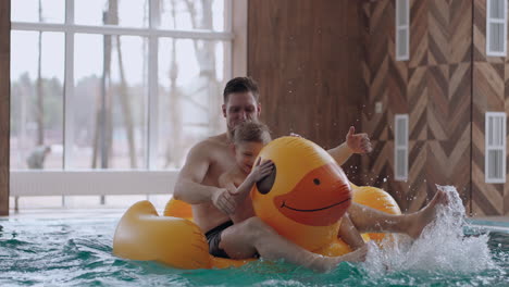 family entertainment in swimming pool father and little son are floating on funny rubber duck and laughing