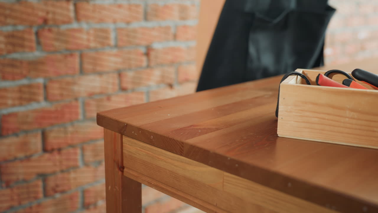 Decorator with blonde hair in orange shirt wearing black apron against rustic brick wall, with dried flower decorations in glass vases, preparation and design