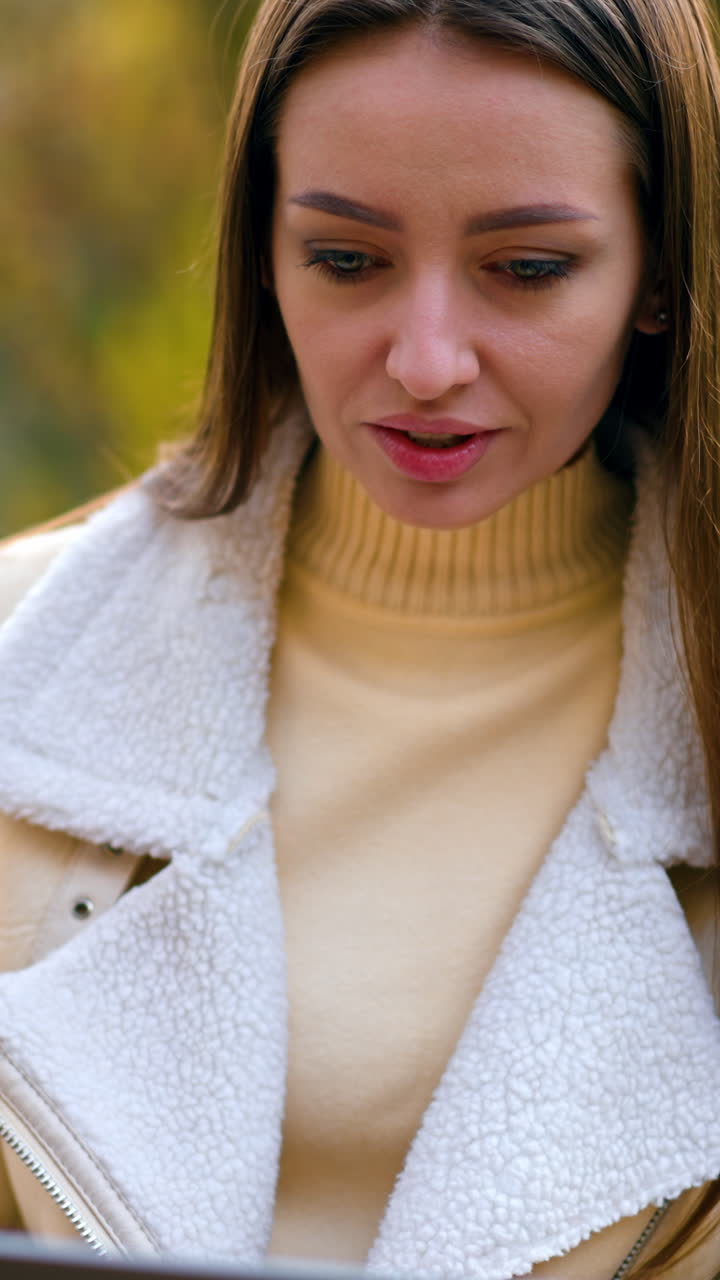 Modern young woman using laptop sitting in the nature. Brunette beautiful lady sitting on the table looking at computer screen. Autumn nature backdrop. Vertical video